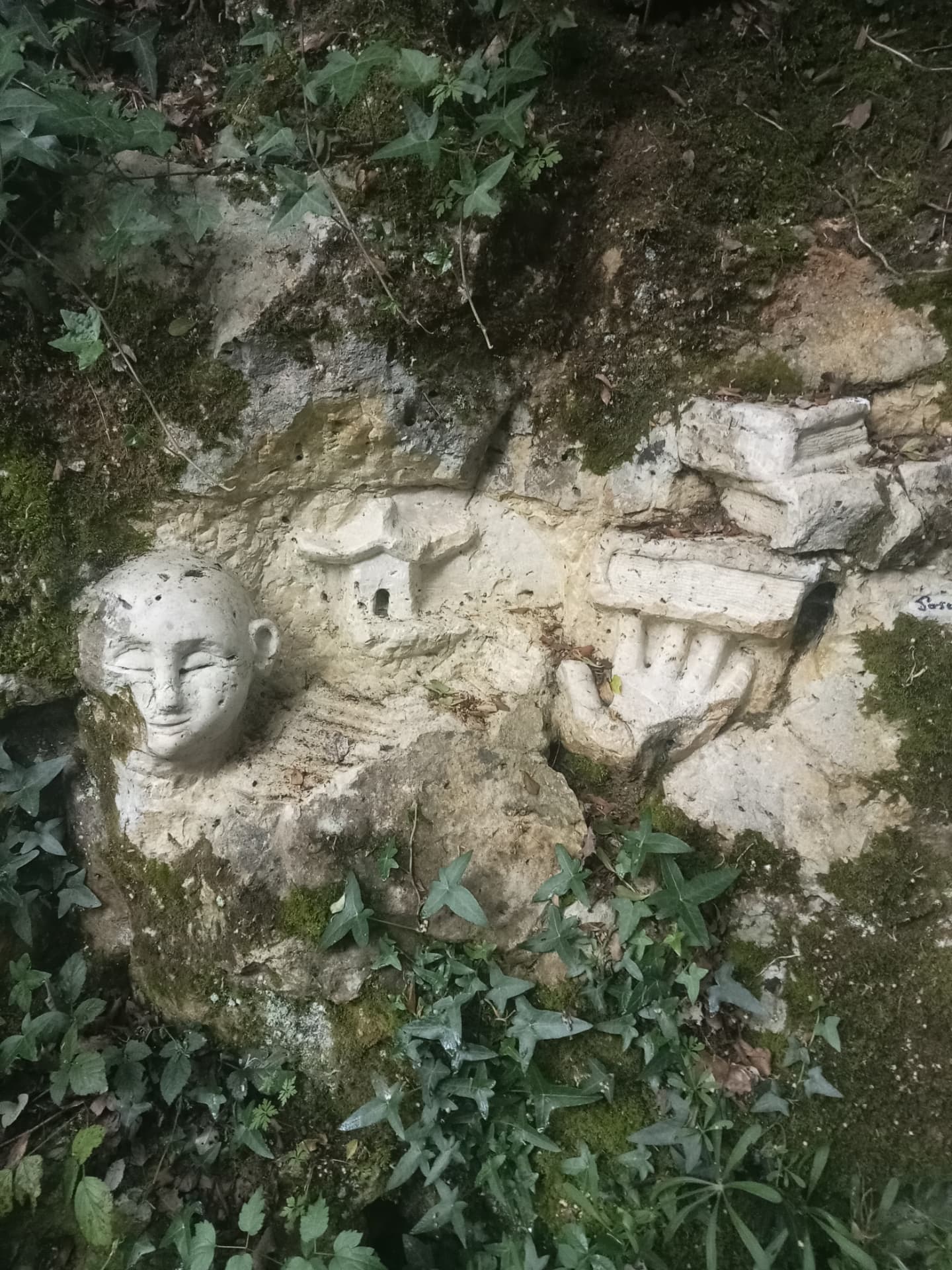 Ensemble sculpté d'un visage, d'une maison et d'une main dans un muret calcaire