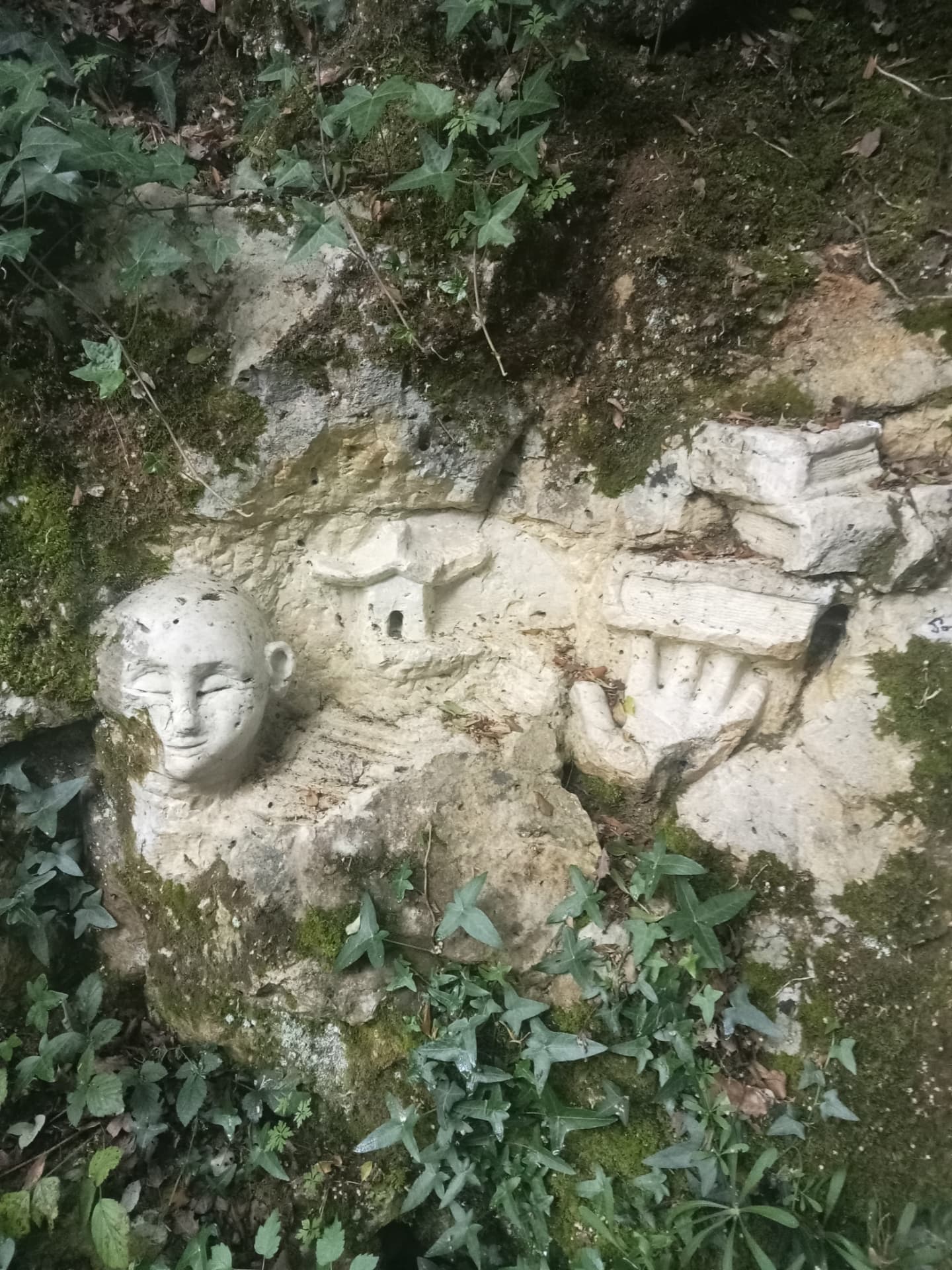 Visage souriant, petite maison et main ouverte sculptés dans la pierre