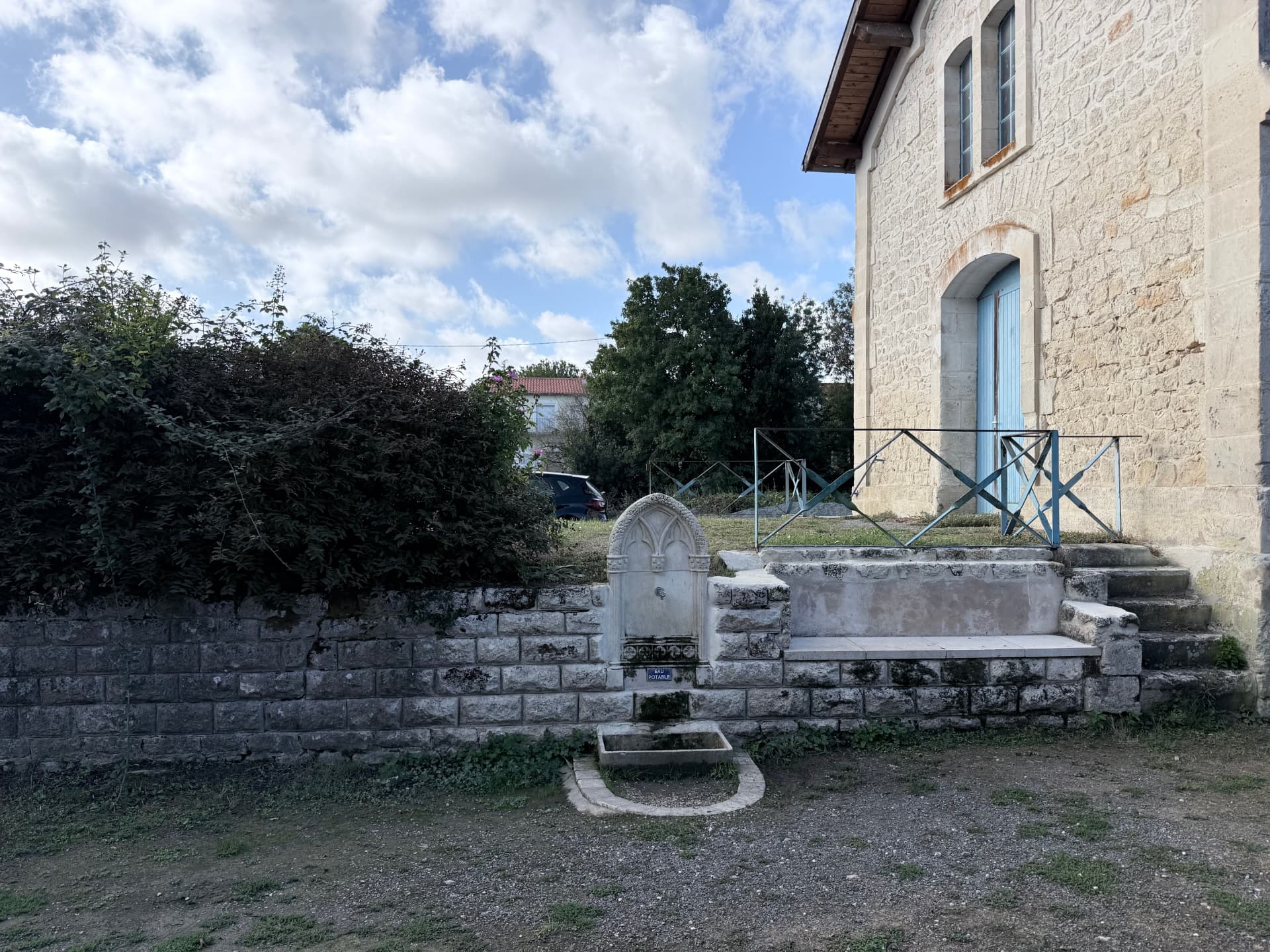 Fontaine d'eau potable en pierre adossée au mur, devant l'ancien bâtiment de la gare de Saint-Agnant